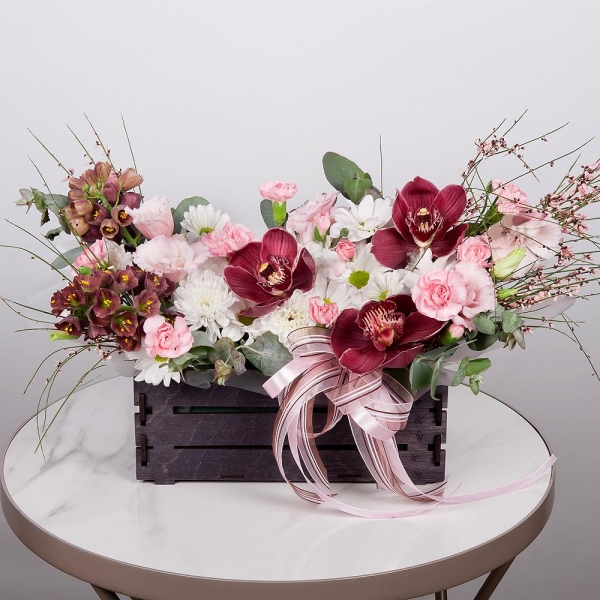 Pink Cymbidium Orchid Bud - 3, Baltica White Spray Chrysanthemum - 1, Pink Lisianthus (Eustoma) - 3, Pink spray carnation - 3, White Delphinium - 2, Bacardi White Spray Chrysanthemum - 1, Wooden pot, Oasis, Wrapping Paper, Flask for orchids, Eucalyptus, Genista
